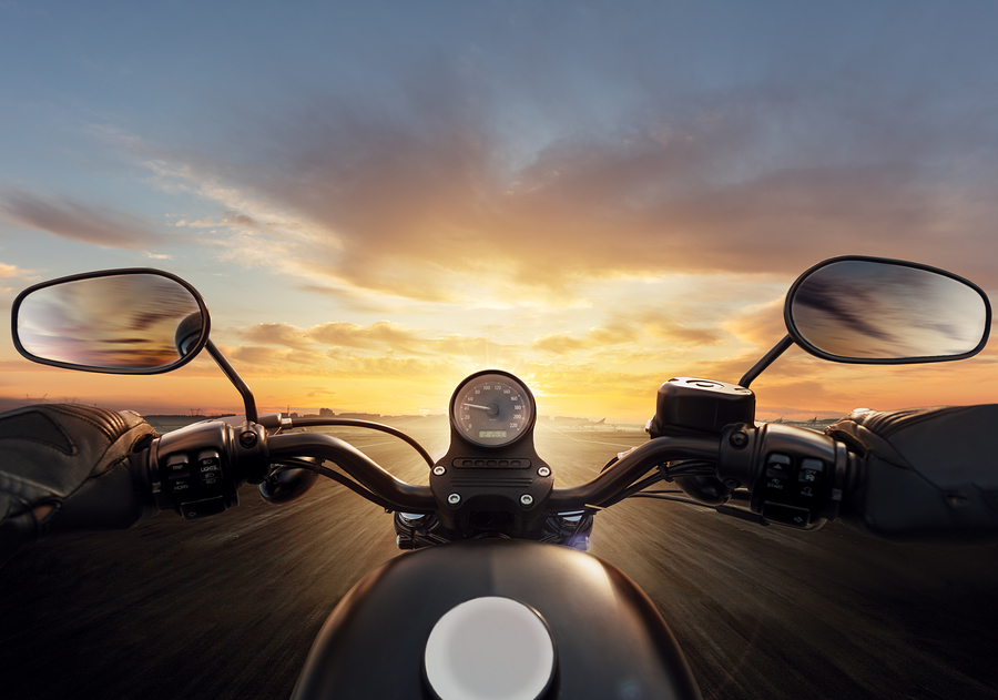 Motorcycle driving down the road lit by the sunset.