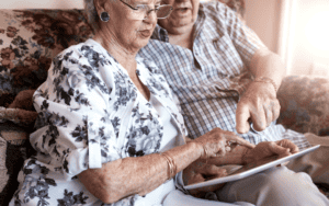 An elderly couple seated, using a tablet