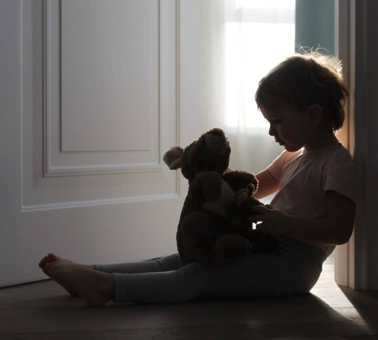 Child sitting in doorway holding stuffed animal